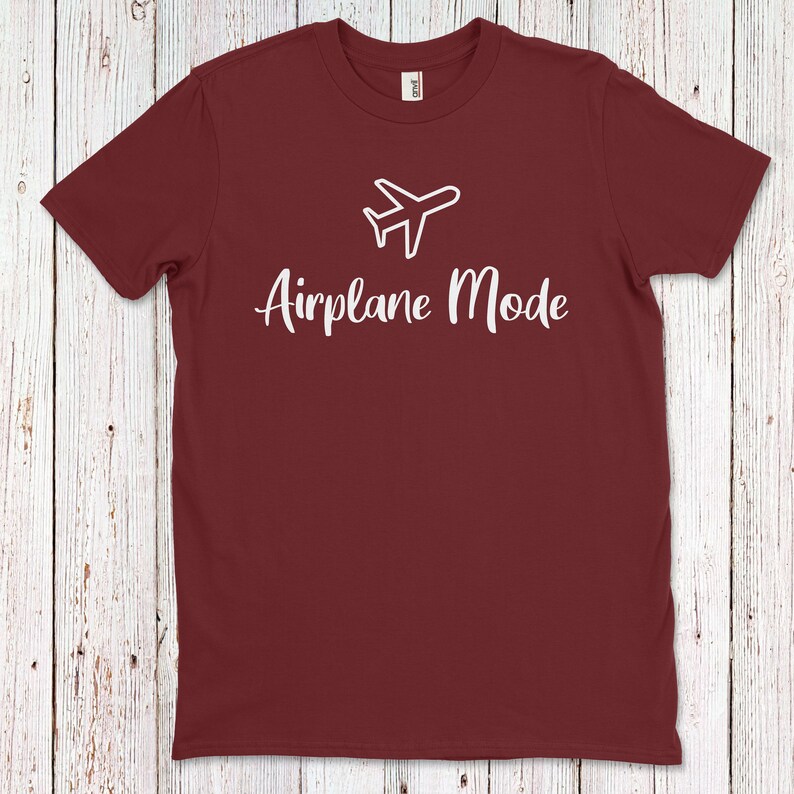 Op de afbeelding: Een maroon t-shirt met een witte vliegtuigafbeelding en de tekst "Vliegtuigmodus" erop gedrukt.