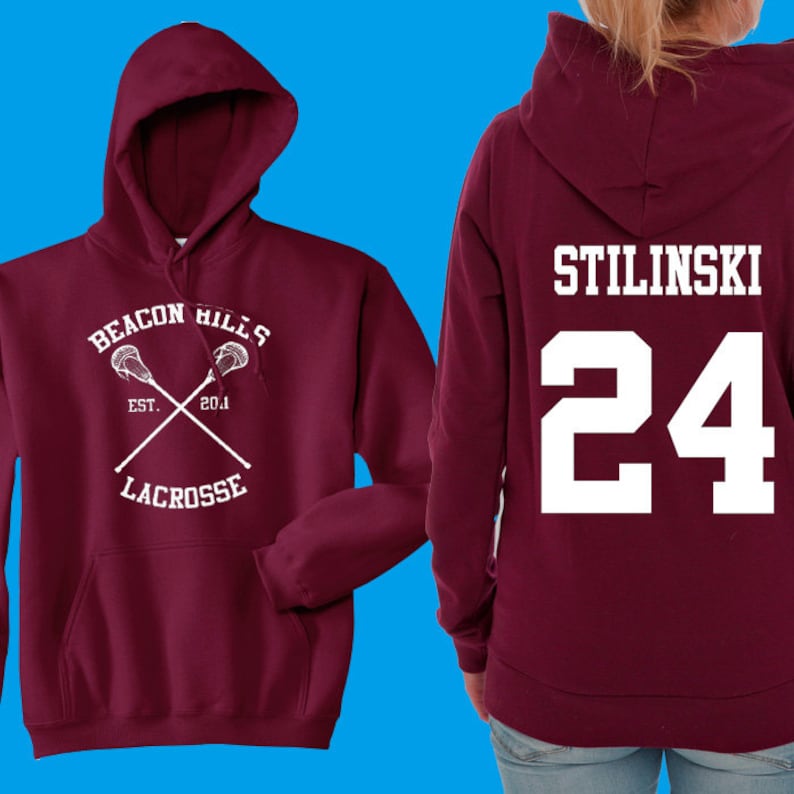 May include: Burgundy hooded sweatshirt with a white lacrosse stick design on the front and the text "Beacon Hills Est. 2014 Lacrosse" and the text "Stilinski 24" on the back.
