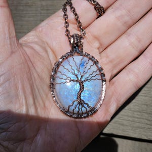 May include: A copper wire wrapped tree of life pendant with a moonstone cabochon. The pendant is oval shaped and has a copper chain.