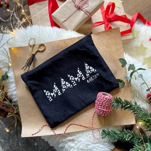 May include: Black canvas zippered pouch with the word "MAMA" in white letters with a white polka dot pattern. The text "est. 2014" is in white letters below the word "MAMA". The pouch is on a brown paper surface with red and white twine.