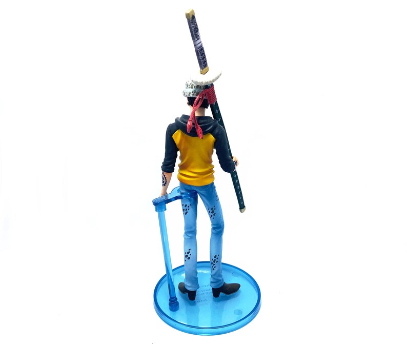 Pu&ograve; includere: Statuetta dettagliata di un personaggio della serie anime One Piece. La figura indossa una felpa con cappuccio gialla e nera, jeans blu e una bandana rossa. Tiene una katana e si trova su una base circolare blu.