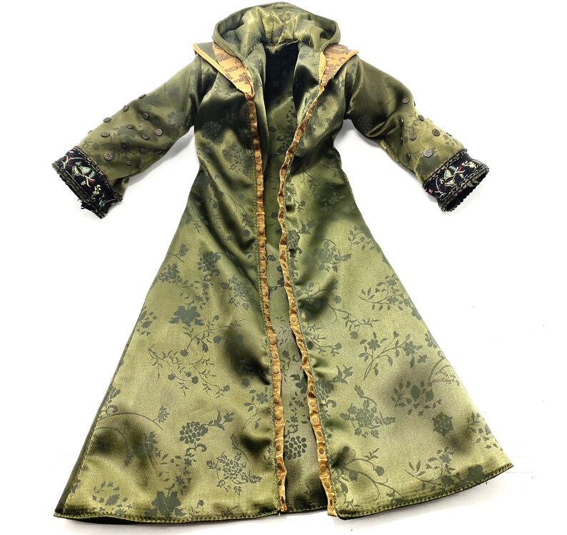 Op de afbeelding: Een lange groene satijnen robe met een bloemenpatroon, gouden bies en een capuchon. De robe heeft een decoratief ontwerp op de mouwen.