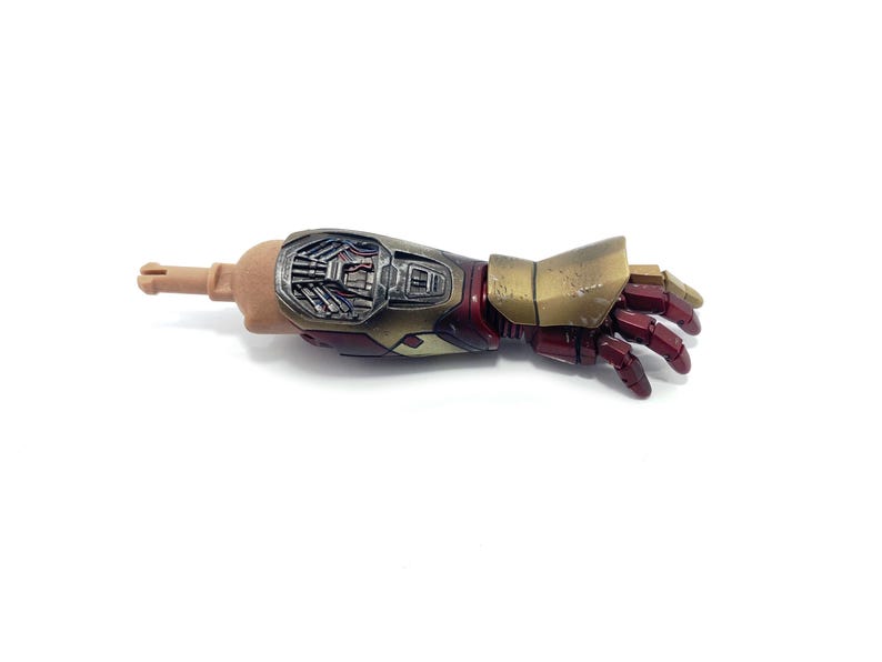 K&ouml;nnte beinhalten: Ein detaillierter Actionfigurenarm, mit einem hellbraunen Oberarm und einem metallischen Unterarm und Hand. Der Unterarm ist eine Mischung aus Silber, Gold und Rot, mit aufwendigen mechanischen Details. Die Hand ist tiefrot.