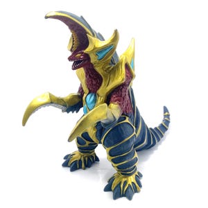 May include: A red and gold monster figure with a large horn and sharp claws. The figure is posed in a standing position with its claws raised.