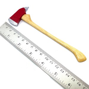 Pode incluir: Um machado de bombeiro de brinquedo vermelho e prateado com cabo de madeira. O machado tem aproximadamente 30 cm de comprimento e est&aacute; ao lado de uma r&eacute;gua para escala.