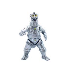 Puede incluir: Figura de robot plateado con un diseño detallado, con una cabeza en forma de corona y ojos amarillos. La figura tiene brazos y piernas articulados, y una expresión amenazante. El robot está sobre una superficie blanca.