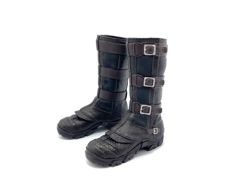 May include: A pair of black leather boots with brown straps and buckles. The boots have a textured surface and a chunky sole.