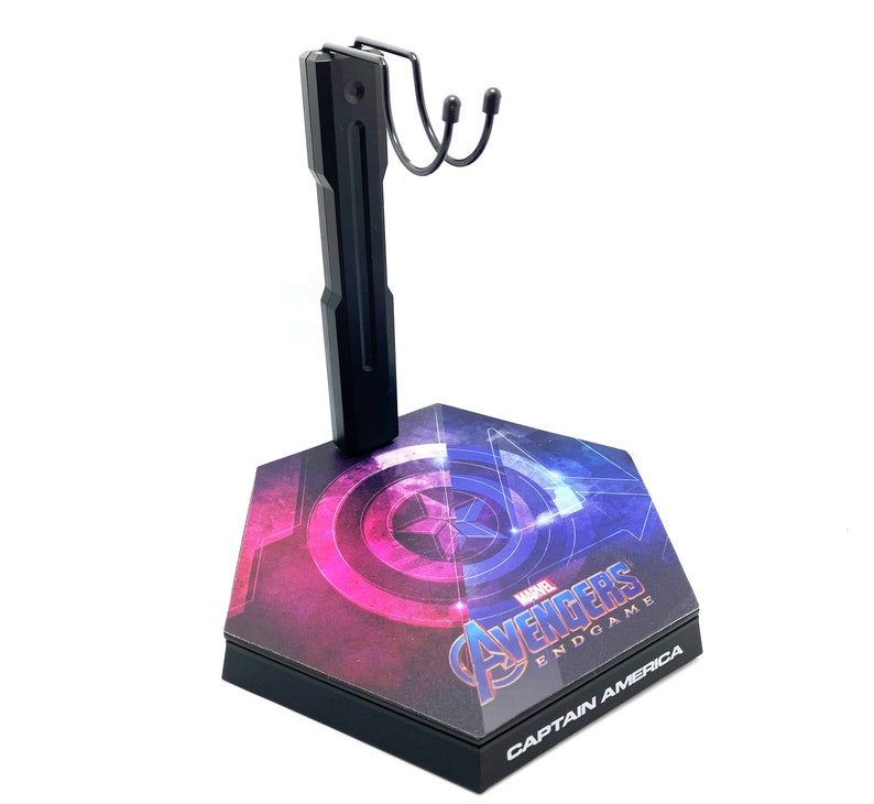 K&ouml;nnte beinhalten: Schwarzer Actionfigurenst&auml;nder mit Captain America Endgame-Motiv. Der St&auml;nder hat einen schwarzen Metallarm mit einem Haken und eine Basis mit einer Grafik von Captain Americas Schild und dem Avengers Endgame-Logo.