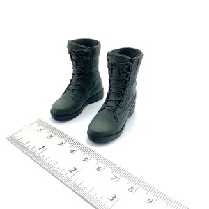 May include: A pair of dark green military-style boots with laces. The boots are about 2.5 inches tall and are sitting on a white surface next to a ruler.
