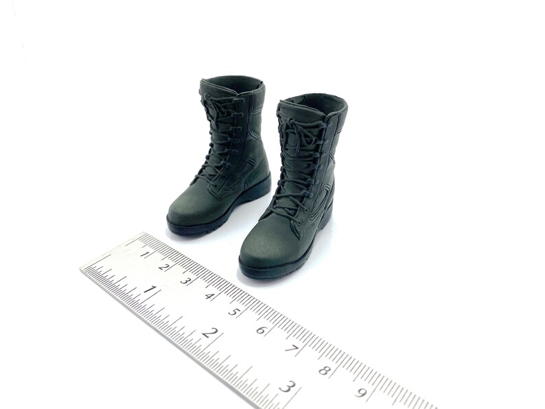 May include: A pair of dark green military-style boots with laces. The boots are about 2.5 inches tall and are sitting on a white surface next to a ruler.