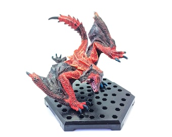 May include: A red and black dragon figurine with outstretched wings and an open mouth, mounted on a black hexagonal base. The dragon has detailed scales and claws, with a dynamic pose. The figurine is set against a white background.