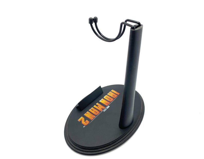 May include: Black plastic action figure stand with a metal arm and a circular base. The base has the words "Iron Man 2" printed on it.