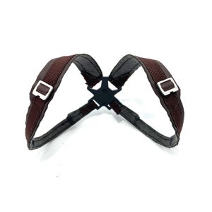 May include: A brown harness with silver buckles and a black star-shaped connector. The harness is made of a woven material and is designed to be worn on the upper body.