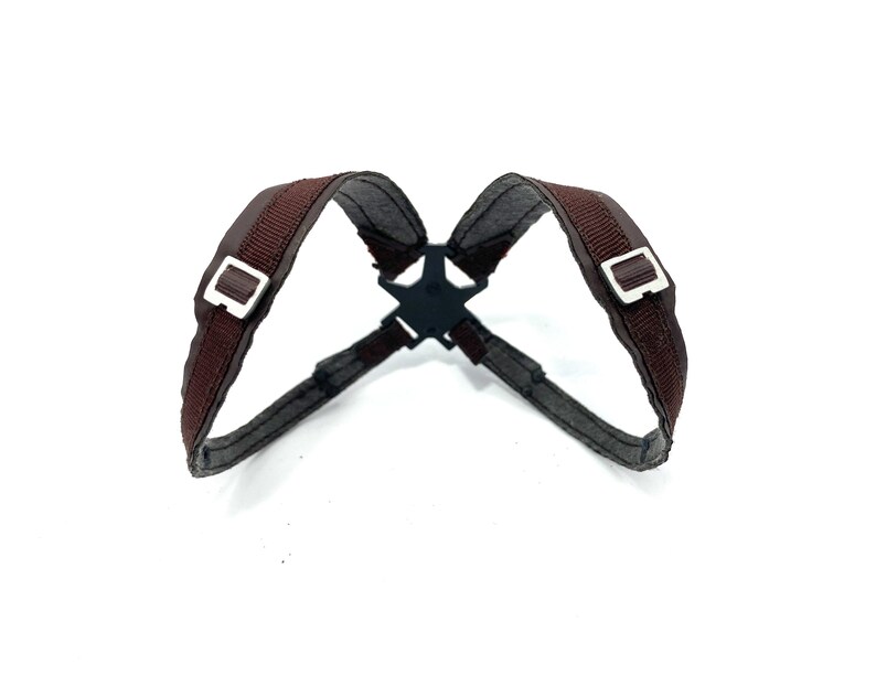 May include: A brown harness with silver buckles and a black star-shaped connector. The harness is made of a woven material and is designed to be worn on the upper body.