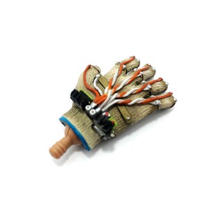 Puede incluir: Un guante marr&oacute;n y beige con cables naranja y blanco unidos a &eacute;l. El guante tiene una superficie texturizada y un pu&ntilde;o azul. El guante est&aacute; unido a una mano marr&oacute;n y beige.