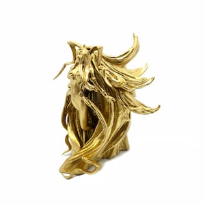 May include: A gold-colored sculpture of a woman with flowing hair and drapery. The sculpture has a classical design, with the woman's profile visible. The piece is set against a white background, highlighting its intricate details.