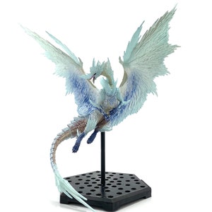 May include: A detailed dragon figurine, predominantly white with blue detailing, mounted on a black stand. The dragon has large, outstretched wings, and is posed mid-flight. The base is hexagonal. The wings have intricate feather details.