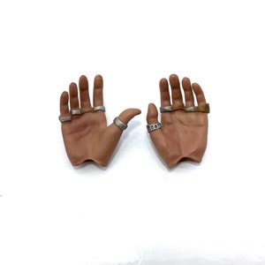 Puede incluir: Dos manos de aspecto realista con anillos de plata en los dedos. Las manos est&aacute;n posadas como si estuvieran abiertas y listas para recibir algo.