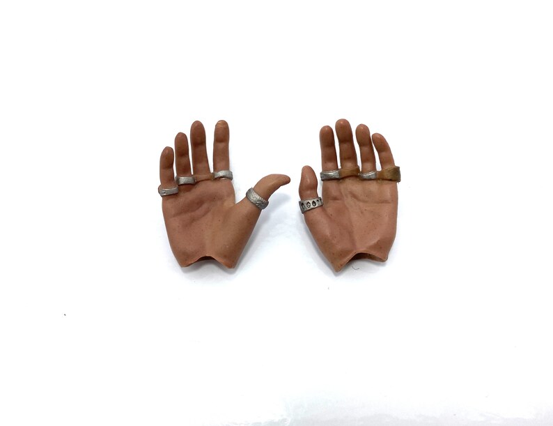 Puede incluir: Dos manos de aspecto realista con anillos de plata en los dedos. Las manos est&aacute;n posadas como si estuvieran abiertas y listas para recibir algo.