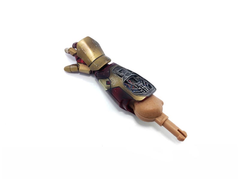 K&ouml;nnte beinhalten: Ein detaillierter Actionfigurenarm mit metallisch goldener und roter Farbgebung. Der Arm weist komplizierte mechanische Details und eine hellbraune Hand auf. Die Figur ist vor einem wei&szlig;en Hintergrund platziert.
