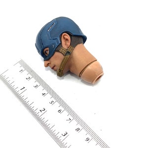 Op de afbeelding: Een Captain America actiefiguur hoofd, met een blauwe helm en een bruine riem. Naast het hoofd ligt een liniaal met centimeter metingen.