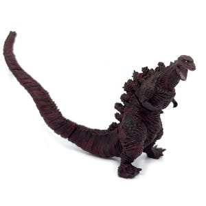 May include: A maroon Godzilla action figure with a long tail and dorsal fins. The figure is in a dynamic pose with its mouth open, showcasing detailed textures and a menacing expression. The figure is on a white background.