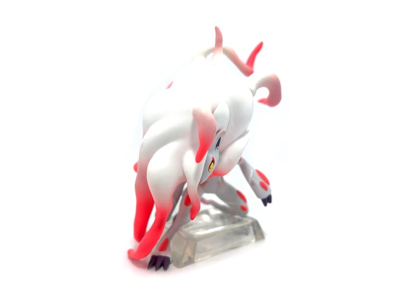 Puede incluir: Figura blanca y roja de una criatura m&iacute;tica en posici&oacute;n agachada. La figura tiene un cuerpo blanco con detalles rojos en las orejas, patas y cola. Est&aacute; colocada sobre una base rectangular transparente.