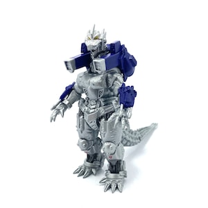 May include: A silver and blue action figure of a robotic monster with a spiky head, a long tail, and blue shoulder-mounted cannons. The figure has intricate mechanical details and the text "MDF-3" on its chest.