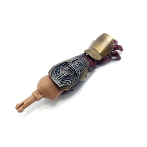 K&ouml;nnte beinhalten: Ein detaillierter Actionfigurenarm mit metallischer Gold- und Burgunder-Farbgebung. Der Arm weist komplizierte mechanische Details und einen hellbraunen Aufsatz auf. Die Hand befindet sich in einer teilweise geschlossenen Position, was auf eine dynamische Pose hindeutet.