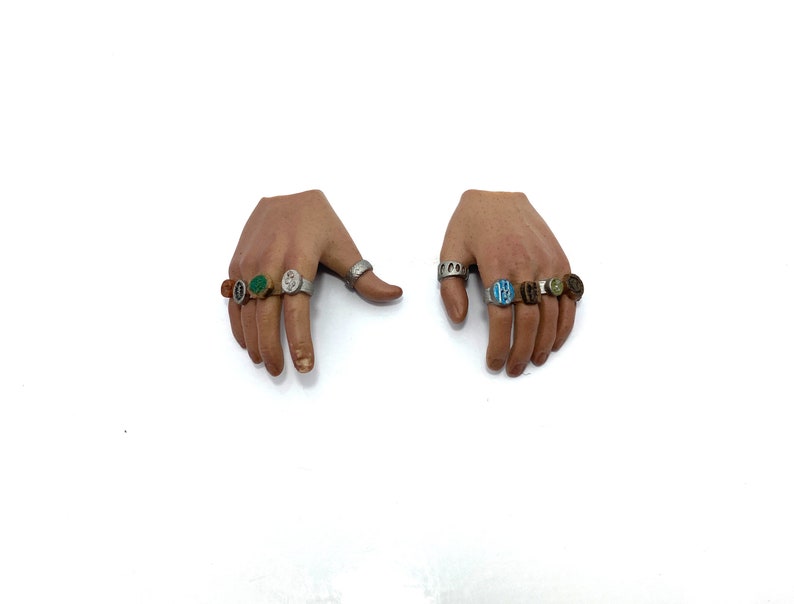 Puede incluir: Dos manos con m&uacute;ltiples anillos en cada dedo. Los anillos son de plata con piedras de diferentes colores, incluyendo verde, azul y marr&oacute;n.