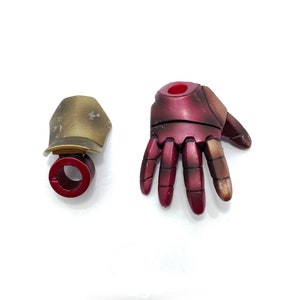 May include: A red and gold plastic hand and a gold plastic wrist piece. The hand has five fingers and a red center. The wrist piece has a red ring around the center.