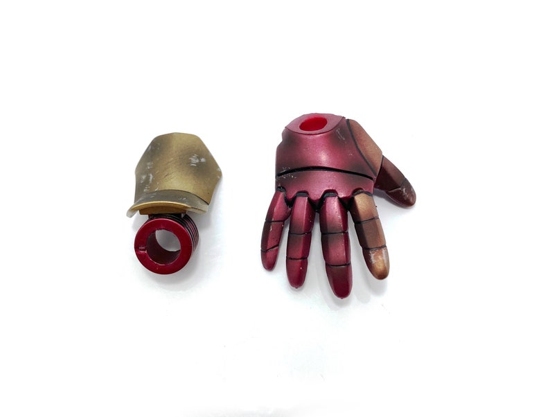 May include: A red and gold plastic hand and a gold plastic wrist piece. The hand has five fingers and a red center. The wrist piece has a red ring around the center.