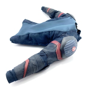 Op de afbeelding: Een zwart en blauw action figure-kostuum met rode accenten en een grijze gevoerde elleboogbeschermer. Het kostuum heeft een textuurstof en een klein rood cirkellogo op de elleboogbeschermer.