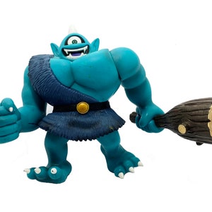 May include: A blue one-eyed cyclops toy figure with a club, wearing a blue and brown loincloth and a gold belt.