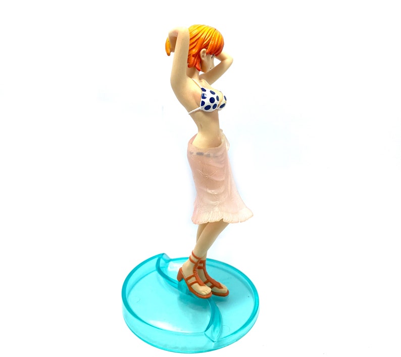 May include: A figurine of a woman with orange hair wearing a pink skirt and a blue and white polka dot bikini top. She is standing on a blue and white base.