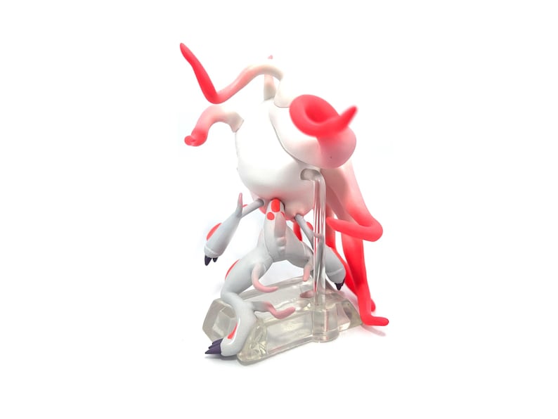 Puede incluir: Una figura blanca y roja de una criatura con un cuerpo esbelto, cuernos curvos y ap&eacute;ndices fluidos en forma de tent&aacute;culos. La figura est&aacute; posada sobre una base rectangular transparente. La paleta de colores incluye blanco, rojo y toques de gris.