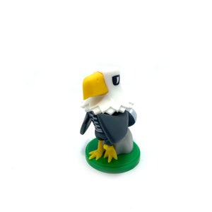 Peut inclure: Une petite figurine d'aigle blanche et grise avec un bec jaune et des yeux noirs. La figurine est posée sur une base verte.