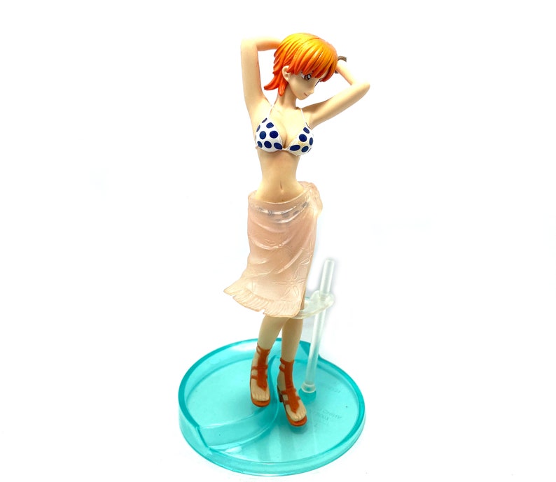May include: A figurine of a woman with orange hair wearing a blue and white polka dot bikini and a pink sheer skirt. She is standing on a blue and white base.