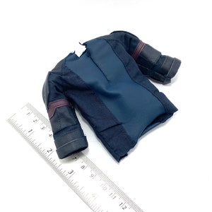 Puede incluir: Una camisa negra y azul oscuro para figura de acci&oacute;n con detalles burdeos y tejido texturizado. La camisa tiene una cremallera en la parte delantera y un peque&ntilde;o desgarro en el hombro.