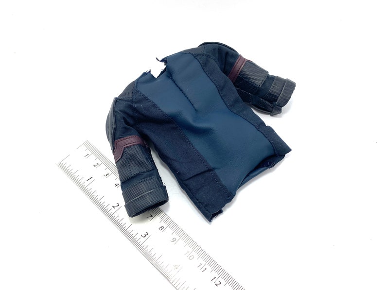 Puede incluir: Una camisa negra y azul oscuro para figura de acci&oacute;n con detalles burdeos y tejido texturizado. La camisa tiene una cremallera en la parte delantera y un peque&ntilde;o desgarro en el hombro.