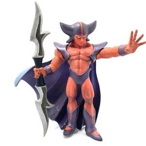 May include: A red and purple action figure of a muscular humanoid character with a horned helmet, cape, and spear. The figure has a stern expression and is posed with one hand raised.