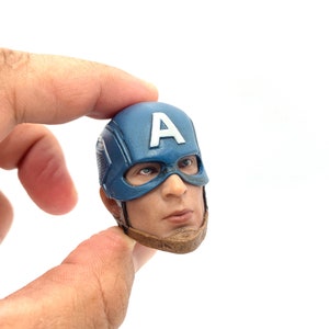 Puede incluir: Una escultura de cabeza de pl&aacute;stico azul y marr&oacute;n de Capit&aacute;n Am&eacute;rica, con su ic&oacute;nico casco con una "A" blanca en la parte delantera. El casco tiene una m&aacute;scara azul con una franja blanca sobre los ojos.