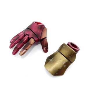 May include: Two action figure hands, one red and gold, the other gold. The red hand is open with fingers spread. The gold hand is closed with the fingers curled.