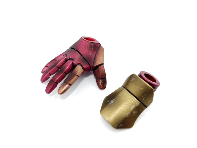 May include: Two action figure hands, one red and gold, the other gold. The red hand is open with fingers spread. The gold hand is closed with the fingers curled.