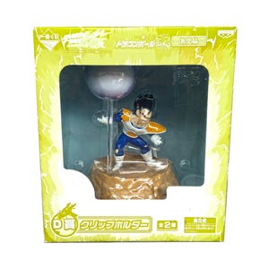 May include: A Dragon Ball Z figure of Vegeta in a dynamic pose, displayed in a clear plastic case. The figure is detailed with blue, white, and gold armor. The packaging is yellow with Japanese text.