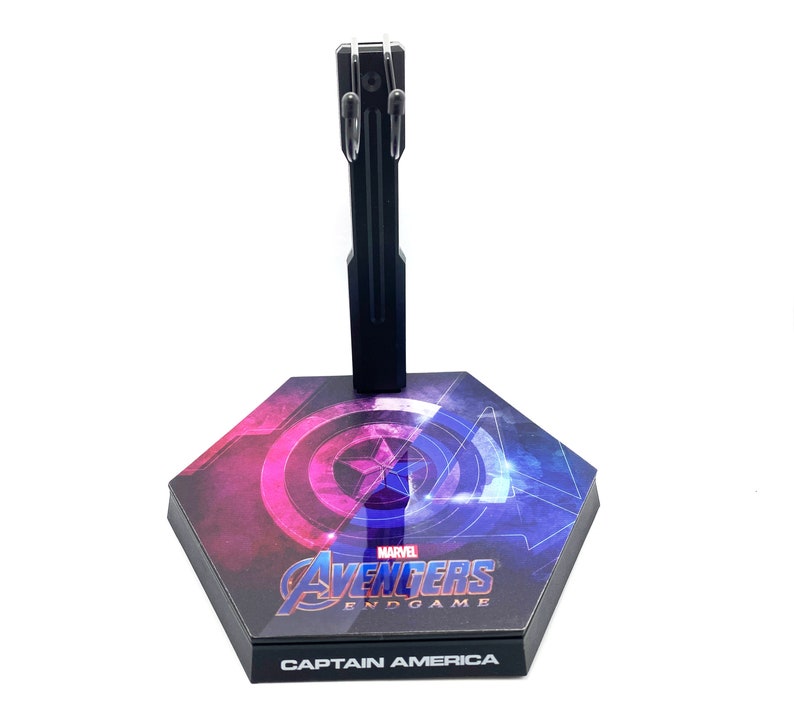 K&ouml;nnte beinhalten: Ein schwarzer Plastik-Actionfigurenst&auml;nder mit sechseckiger Basis. Die Basis zeigt eine Grafik von Captain Americas Schild mit den Worten "Marvel Avengers Endgame" und "Captain America" darauf.
