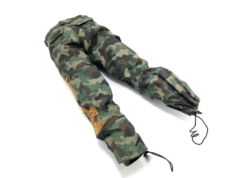 May include: Camouflage trousers with a drawstring at the bottom of the legs. The trousers have a gold embroidered design on the left leg.