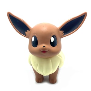 May include: A brown and cream coloured Eevee Pokemon figurine with black ears and brown eyes.