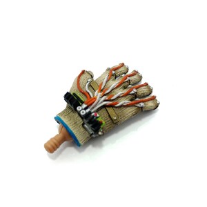 Puede incluir: Una mano rob&oacute;tica beige y marr&oacute;n con cables naranja y blanco. La mano est&aacute; hecha de pl&aacute;stico y tiene un dise&ntilde;o realista.