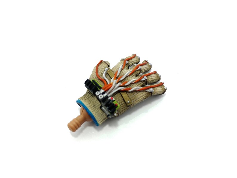 Puede incluir: Una mano rob&oacute;tica beige y marr&oacute;n con cables naranja y blanco. La mano est&aacute; hecha de pl&aacute;stico y tiene un dise&ntilde;o realista.
